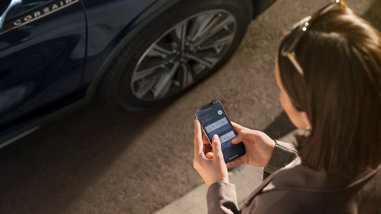 A woman looking down at her phone in front of her car.